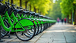 © Pete - Park bike station with many bright green bikes ready for rent. Eco-friendly public transport option. People walk by. Healthy lifestyle choice. Urban environment. Summer day. City park setting.