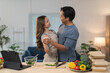 © crizzystudio - Happy young asian couple dancing in kitchen while preparing healthy meal together, enjoying romantic moment at home, vegetables on table, tablet on table, delivery food boxes on table