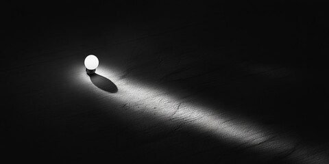 Sticker - A single light bulb on a dark surface, casting a long shadow, creating a minimalist and dramatic atmosphere.