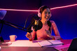 © Summit Art Creations - Smiling creative young beautiful Asian influencer talking in channel with positive podcast speech at night time, using laptop for presentation online at pink neon light modern studio. Stratagem.