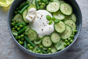 Wall Mural - Bowl of salad with burrata cheese, fresh cucumber, green peas, beans and basil, horizontal shot, middle closeup