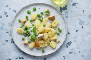 Wall Mural - Plate of italian gnocchi served with cheese and green peas, horizontal shot on a white and blue granite background, high angle view