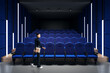© Who is Danny - Modern theater interior with blue seats and a woman walking by.