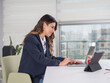 © Designerant - Using laptop, side view image of young caucasian brunette business woman using laptop sit desk at office near window. Wear formal navy blue jacket doing work smiling positive female office worker.