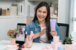 © Summit Art Creations - Young beautiful Asian girl reviewing moisturizing body lotion cream product to make glow skin testing on arm on social media online live recording smartphone with bestseller at modern room. Stratagem.