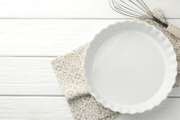 Poster - Ceramic casserole and whisk on white wooden table, top view. Space for text