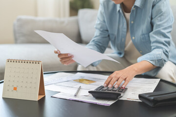 Wall Mural - Stressed asian young business woman, employee using calculator to calculate expenses of monthly, hand holding bills and receipt for to payment on table at home. Financial, finance of banking concept.