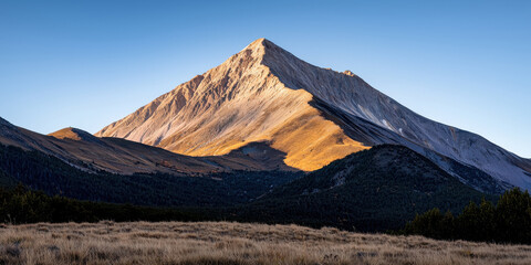 Wall Mural - A majestic mountain peak bathed in golden sunlight, surrounded by rolling hills and a clear blue sky.