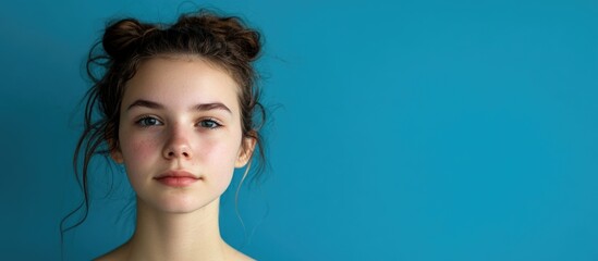 Wall Mural - Frontal portrait of a young woman with natural makeup and tousled hair against a vibrant blue background showcasing empty space for text