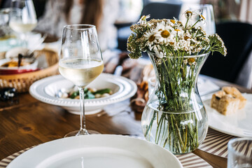 Rustic farm-to-table dining setup with white wine, fresh floral centerpiece, and artisanal food, showcasing natural elegance and homemade meals