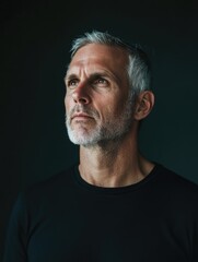 Poster - mature man with short gray hair and beard in black shirt posing thoughtfully against dark background