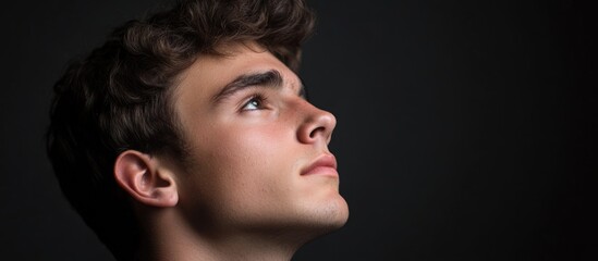 Poster - Young adult male profile portrait in studio setting with dramatic lighting and large empty space for text, showcasing light brown hair and thoughtful expression.