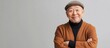 © The 2R Artificiality - Cheerful senior Chinese man in a brown cardigan and gray cap smiling confidently against a soft gray background with ample copy space for text.