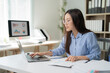 © Tj - Young Asian businesswoman wearing eyeglasses concentrating on working with laptop and analyzing financial charts. Sitting at her desk in modern office. Dedicated to her tasks and striving for success