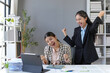 © amnaj - Two Asian businesswomen celebrating their successful deal in a modern office, expressing joy and excitement while collaborating on their project