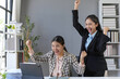 © amnaj - Two euphoric asian businesswomen raising arms and celebrating successful project in modern office