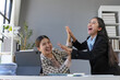 © amnaj - Two happy businesswomen high fiving each other, celebrating a successful project or achievement in a modern office
