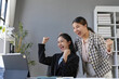 © amnaj - Two asian businesswomen celebrating a successful project while looking at a tablet in a modern office