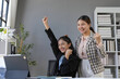 © amnaj - Two asian businesswomen are celebrating a successful project in the office, raising their arms in excitement