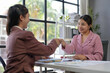 © amnaj - Two smiling businesswomen shaking hands after reaching an agreement during a business meeting in a modern office