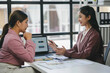 © amnaj - Two Asian businesswomen are discussing marketing strategy using laptop and documents in office