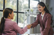 © amnaj - Two smiling businesswomen shaking hands in a modern office, celebrating a successful deal and fostering a strong partnership