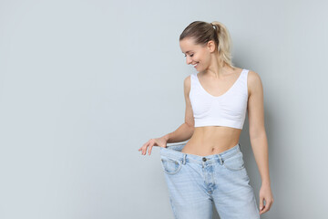 Wall Mural - Weight loss. Happy woman wearing big jeans on light grey background, space for text