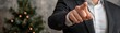 © Chanoknan - A man in a suit points towards the camera with a Christmas tree softly lit in the background, creating a festive atmosphere.
