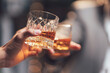 © Kritdanai - Whiskey Toast: Two hands clinking glasses of amber whiskey, a warm, intimate moment captured in soft focus.  A toast to friendship, celebration, or a successful deal.
