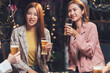 © Kritdanai - Nightlife Cheers: Two stylish Asian women enjoy drinks at a lively evening gathering, sharing laughter and good times with friends. A warm.