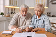 © New Africa - Pension savings. Senior couple planning budget at wooden table indoors