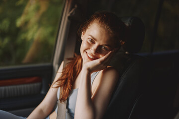 Canvas Print - Young woman smiling while sitting in a car, wearing a casual outfit, conveying happiness in a nature inspired setting