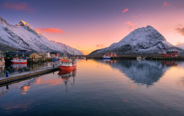 Wall Mural - red fishing boats on the sea, reflection in water, snowy mountains, colorful purple sky with pink cl