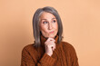 © deagreez - Portrait of a thoughtful mature woman in a brown sweater against a beige background contemplating ideas