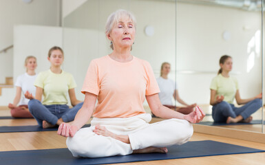 Wall Mural - Closeup of positive elderly woman practice yoga lotus pose to meditation in modern studio