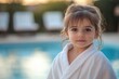 © Fotograf - A young child standing by the side of a pool, wearing a bathrobe and possibly getting ready for a swim