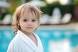 © Fotograf - A young child standing next to a swimming pool, wearing a bathrobe and possibly getting ready for a swim