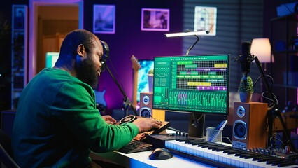 Fototapete - Skilled male composer producing new songs on his mixing console, operating on professional gear in home studio. Artist audio engineer twisting knobs to adjust sound levels on tracks. Camera B.