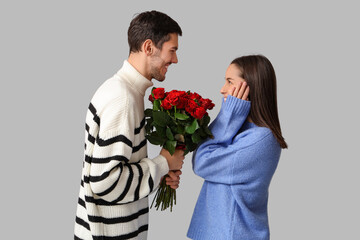 Wall Mural - Beautiful young couple with bouquet of red roses on grey background. Valentine's day celebration