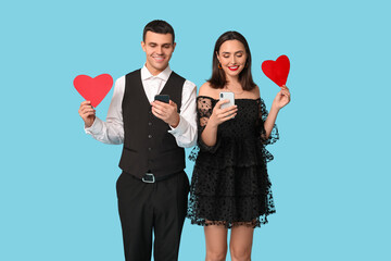 Wall Mural - Young couple with mobile phones and paper hearts on blue background. Online dating