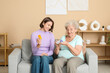 © Pixel-Shot - Young nurse and senior woman with pills sitting on sofa at home