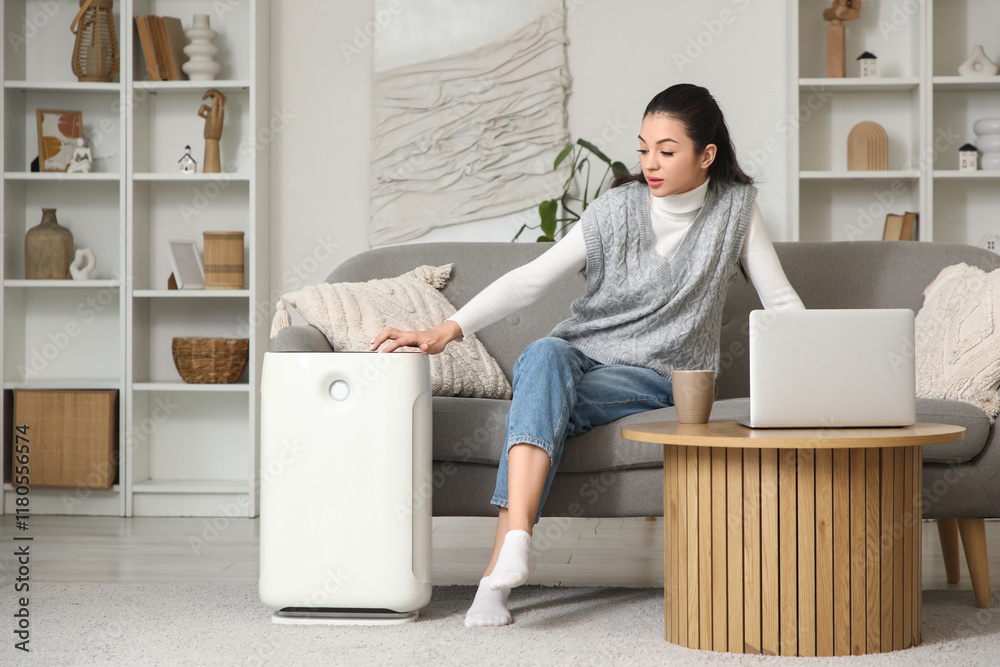 Young woman turning on air purifier at home