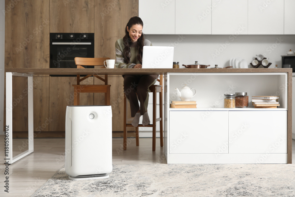 Young woman using laptop with air purifier in kitchen