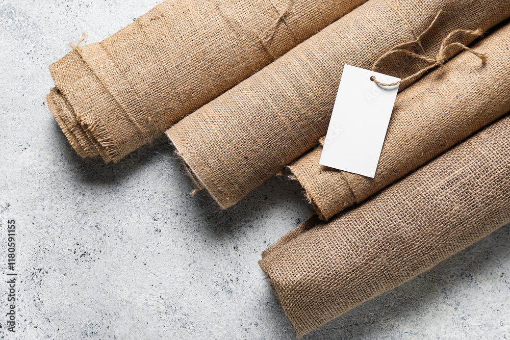 Rolls of burlap fabric and blank shopping tag on light background