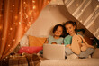 © Pixel-Shot - Cute girls watching cartoons on laptop in hut at night