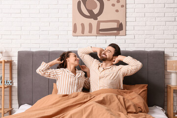 Wall Mural - Happy couple in pajamas stretching on bed at home