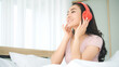 © bixpicture - Young Woman Enjoying Music with Red Headphones While Relaxing at Home. Modern Lifestyle, Entertainment and Relaxation in a Cozy Bedroom Environment.