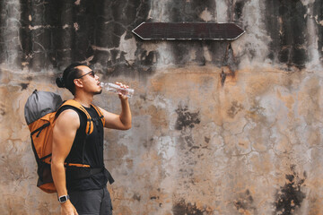 Tourist backpacker drinking bottle of water walking on the hot street in Asia.