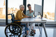 © NDABCREATIVITY - Disabled woman in wheelchair looking at computer, discussing startup project with interracial team