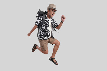 Wall Mural - Excited happy young Asian man tourist wearing backpack and glasses jumping pose.